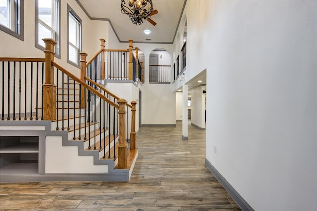 staircase with a high ceiling, crown molding, baseboards, and wood finished floors