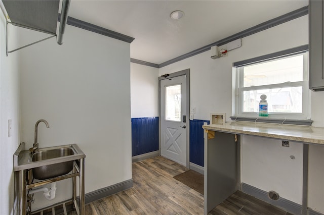 kitchen with dark wood-style floors, a wainscoted wall, crown molding, light countertops, and a sink