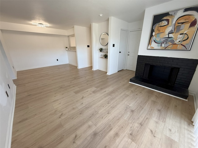 unfurnished living room with light wood-type flooring, a brick fireplace, and baseboards