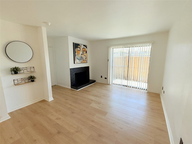 unfurnished living room featuring a fireplace with raised hearth, baseboards, and light wood-style floors