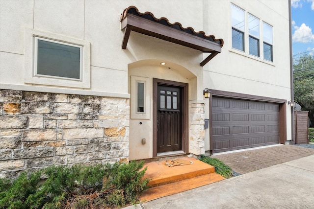 entrance to property with stone siding, an attached garage, driveway, and stucco siding