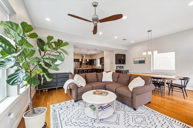 living room featuring baseboards, light wood-type flooring, a ceiling fan, and recessed lighting