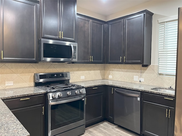 kitchen featuring appliances with stainless steel finishes, light wood-type flooring, light stone counters, and decorative backsplash