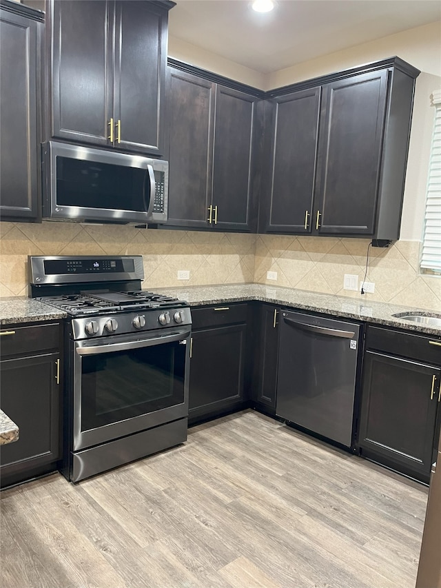 kitchen featuring appliances with stainless steel finishes, decorative backsplash, light wood-style flooring, and light stone countertops