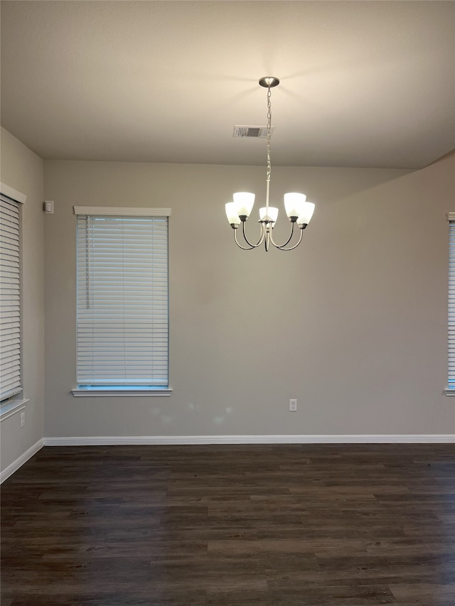 empty room with dark wood-type flooring, visible vents, baseboards, and an inviting chandelier