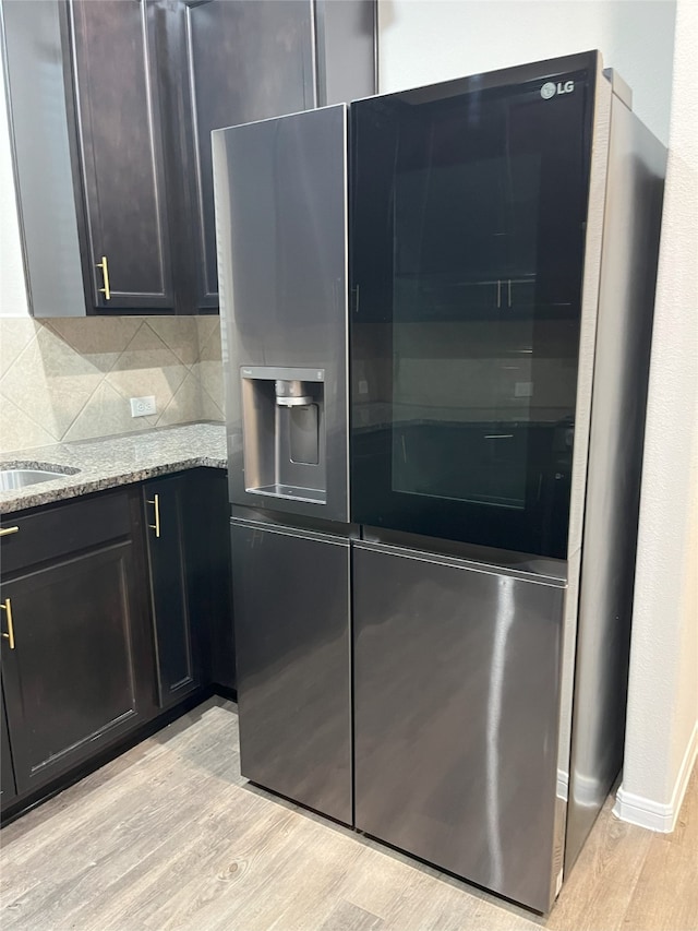 kitchen featuring baseboards, stainless steel fridge with ice dispenser, backsplash, light stone countertops, and light wood finished floors