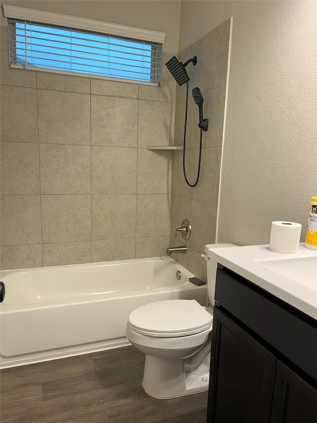 bathroom featuring a textured wall, toilet, wood finished floors, vanity, and shower / washtub combination