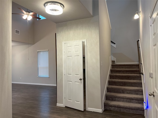 stairway featuring baseboards, visible vents, ceiling fan, wood finished floors, and a high ceiling