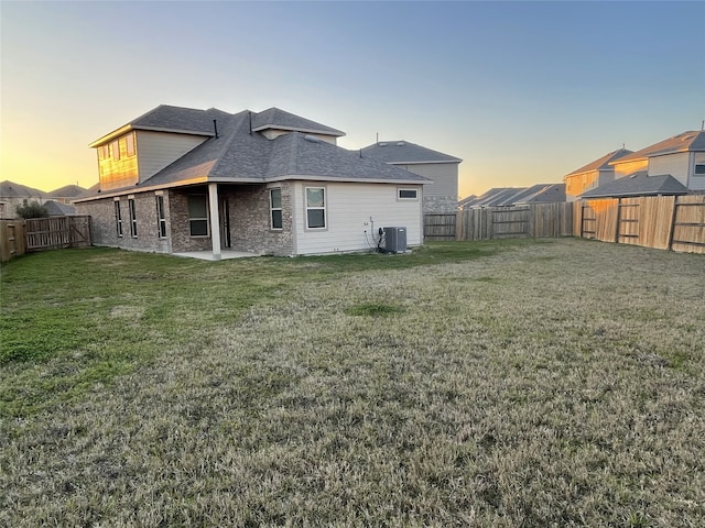 back of house at dusk featuring brick siding, a patio, a lawn, central AC, and a fenced backyard