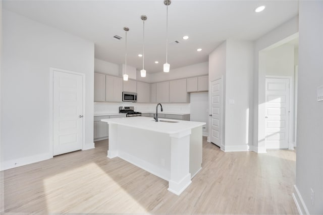 kitchen with a sink, visible vents, appliances with stainless steel finishes, light wood finished floors, and a center island with sink