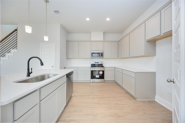 kitchen featuring visible vents, appliances with stainless steel finishes, hanging light fixtures, light wood-style floors, and a sink