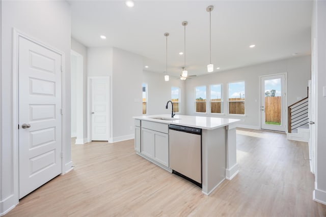 kitchen featuring stainless steel dishwasher, light wood-type flooring, a sink, and pendant lighting