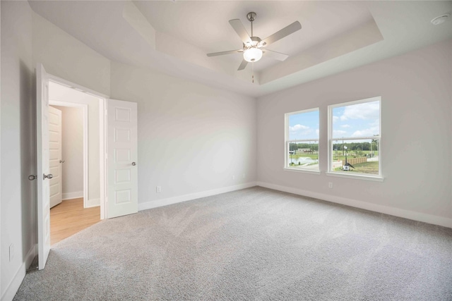 carpeted spare room with baseboards, a tray ceiling, and ceiling fan