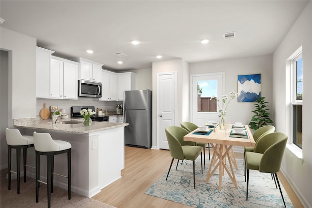 kitchen featuring stainless steel appliances, a peninsula, visible vents, white cabinets, and light stone countertops