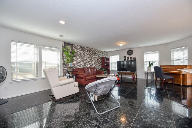 living room with an accent wall, granite finish floor, visible vents, and baseboards