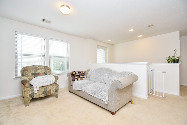 living area with baseboards, an upstairs landing, visible vents, and light colored carpet