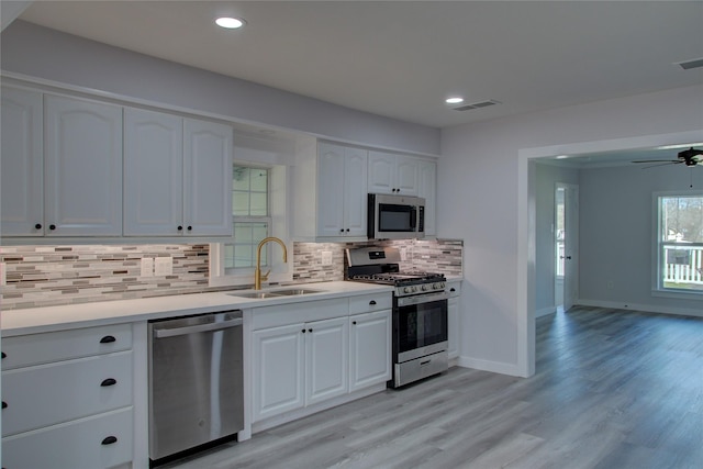 kitchen featuring visible vents, decorative backsplash, appliances with stainless steel finishes, white cabinets, and a sink