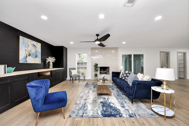 living room featuring a fireplace, a ceiling fan, light wood finished floors, and visible vents