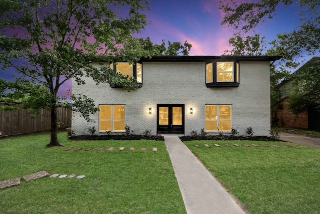 view of front of house featuring a lawn, brick siding, fence, and french doors