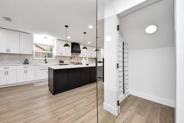 kitchen featuring visible vents, tasteful backsplash, a sink, premium range hood, and light countertops