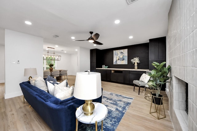 living room featuring visible vents, baseboards, light wood-type flooring, a tile fireplace, and ceiling fan with notable chandelier
