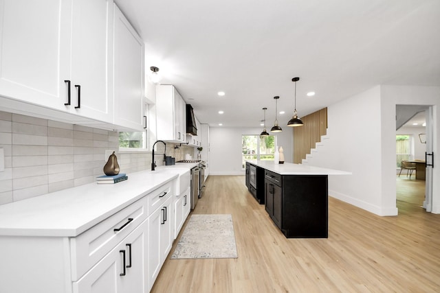 kitchen featuring stainless steel stove, light wood-style floors, light countertops, custom range hood, and a kitchen island
