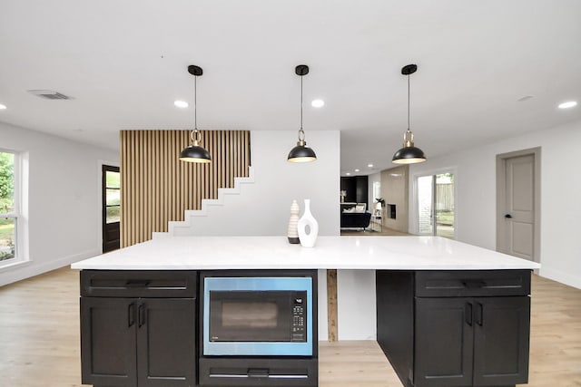 kitchen with light countertops, visible vents, built in microwave, and light wood-type flooring