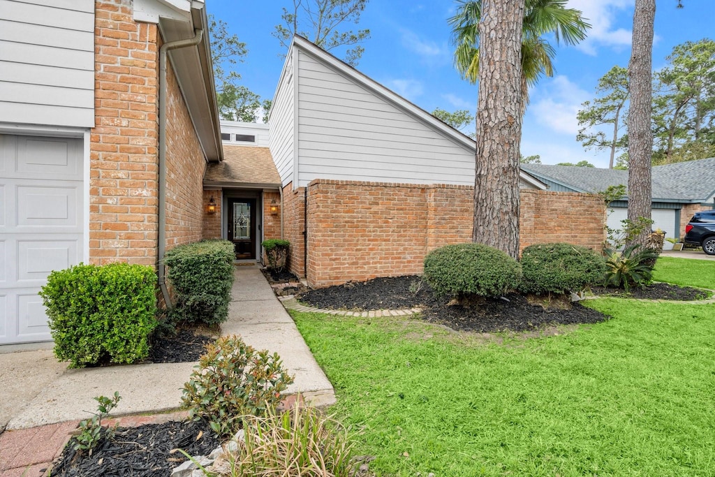 exterior space with brick siding, a lawn, an attached garage, and a shingled roof