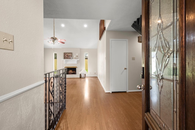 foyer featuring baseboards, a brick fireplace, wood finished floors, and a ceiling fan