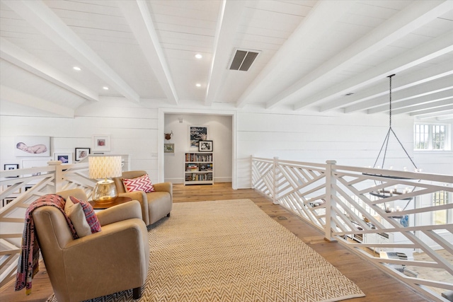 sitting room with beam ceiling, visible vents, light wood-style flooring, and an upstairs landing