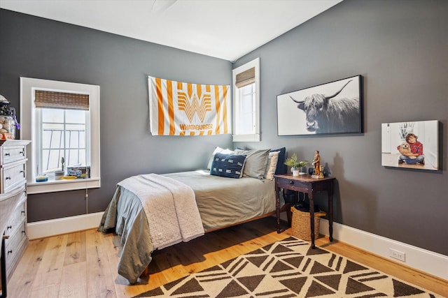 bedroom with light wood finished floors, multiple windows, and baseboards