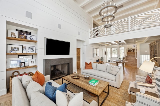 living area featuring a premium fireplace, light wood-type flooring, beam ceiling, and a notable chandelier