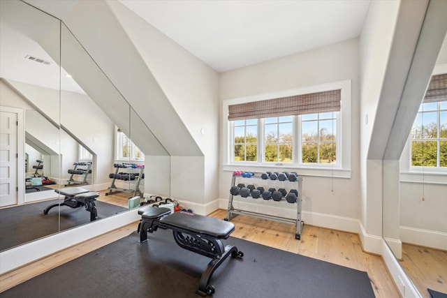 exercise area with lofted ceiling, baseboards, visible vents, and wood finished floors