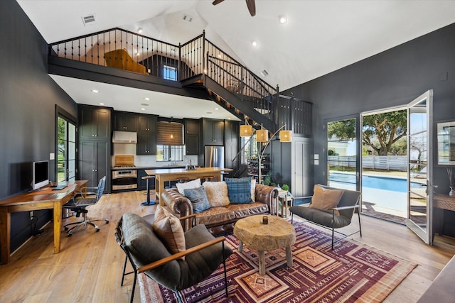 living area featuring high vaulted ceiling, light wood-style flooring, and visible vents