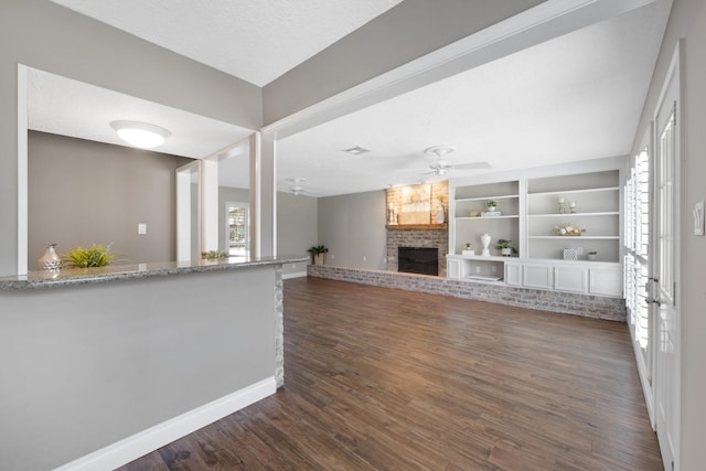 unfurnished living room featuring baseboards, ceiling fan, dark wood-type flooring, a textured ceiling, and a fireplace