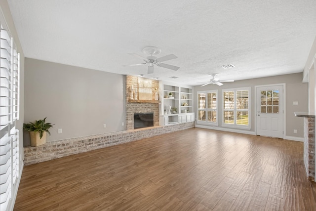 unfurnished living room featuring visible vents, built in features, wood finished floors, a textured ceiling, and a fireplace