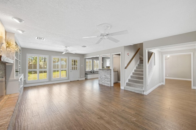 unfurnished living room with ceiling fan, a textured ceiling, wood finished floors, visible vents, and stairs