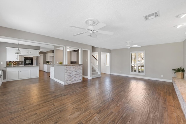 unfurnished living room featuring visible vents, baseboards, dark wood-style floors, ceiling fan, and stairs