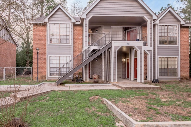 view of front of house featuring brick siding, fence, stairway, and a front lawn