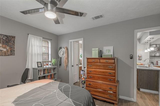 bedroom featuring a textured ceiling, light wood finished floors, a sink, and visible vents