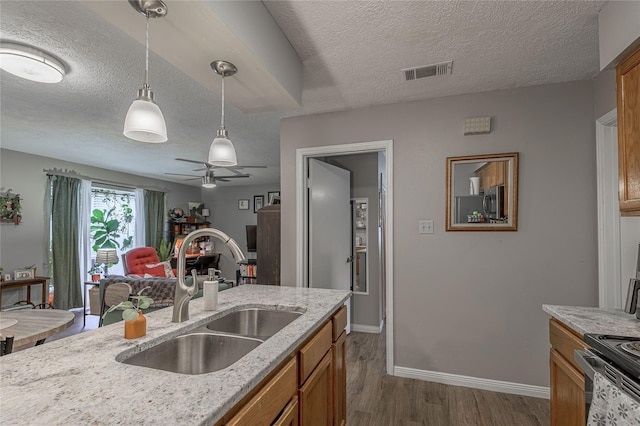 kitchen featuring visible vents, brown cabinets, dark wood-type flooring, decorative light fixtures, and a sink