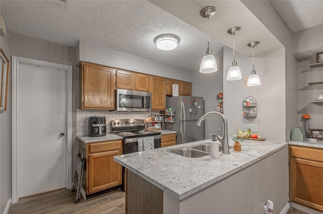 kitchen featuring tasteful backsplash, light wood-style flooring, appliances with stainless steel finishes, a sink, and a peninsula