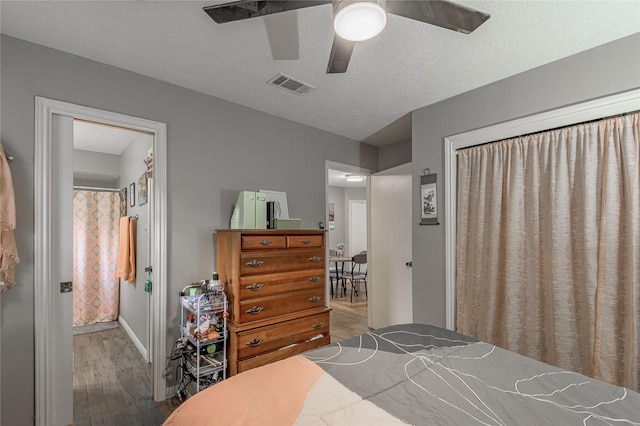 bedroom featuring a ceiling fan, visible vents, a textured ceiling, and wood finished floors