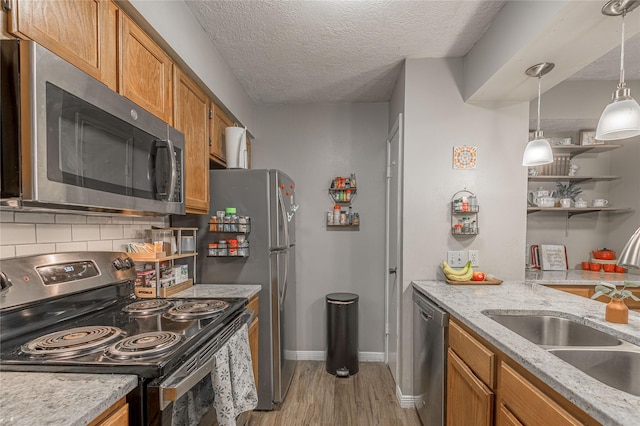 kitchen with tasteful backsplash, appliances with stainless steel finishes, brown cabinets, light wood-style floors, and a sink