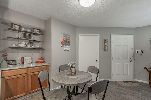 dining room featuring baseboards, a textured ceiling, and light wood finished floors