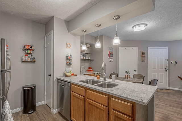 kitchen featuring a peninsula, stainless steel appliances, light wood-style floors, pendant lighting, and a sink