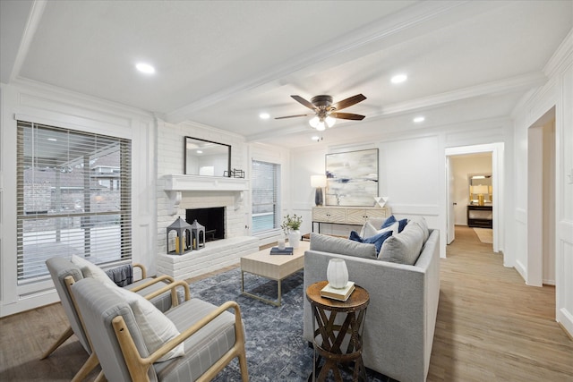 living room with a brick fireplace, ornamental molding, beam ceiling, wood finished floors, and a decorative wall