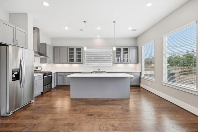 kitchen with dark wood-style floors, stainless steel appliances, gray cabinetry, glass insert cabinets, and wall chimney range hood