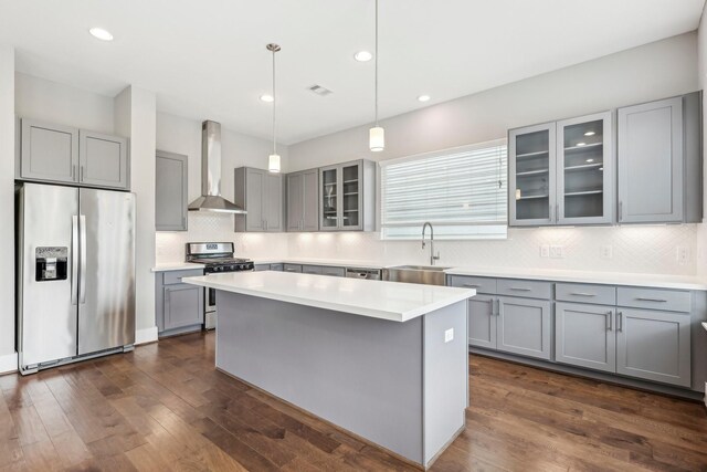 kitchen with appliances with stainless steel finishes, gray cabinets, a sink, and wall chimney range hood