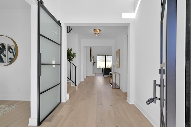 hallway with a barn door, baseboards, stairs, and light wood finished floors